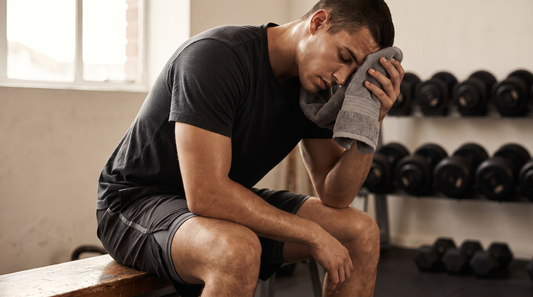 Man on a gym bench pressing a towel to his forehead after a workout