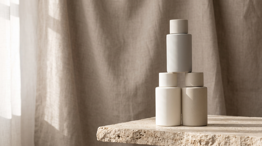 Three plain unlabeled bottles stacked in a small pyramid on a travertine ledge in morning light